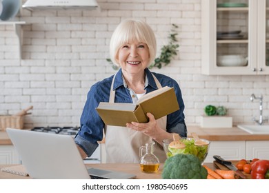 Caucasian aged old senior woman grandmother in apron reading a book of recipes, cooking meal, preparing food in the kitchen. Dieting, healthy eating, cooking at home concept - Powered by Shutterstock