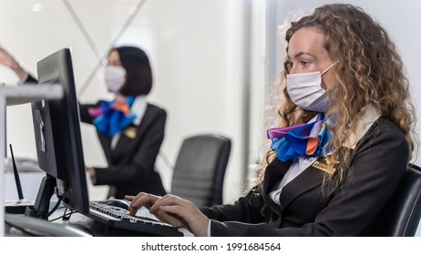 Caucasian Airline Employee  Wearing Face Mask To Prevent Coronavirus Pandemic While Working At Airline Check In Counter In The Airport. Travelling With New Normal Concept.