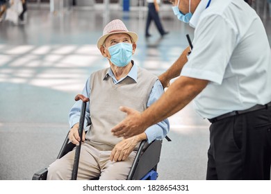 Caucasian Airline Male Employee In A Protective Mask Explaining Something To A Disabled Elderly Man