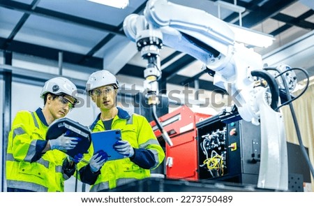 Caucasian american development technician engineer testing artificial intelligence robot arm at high technology research manufactue with equipment. Factory workers working with adept robotic arm.