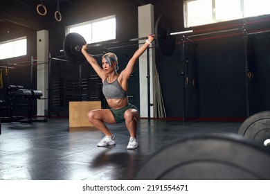 Caucasian Athletic Sport Girl Squatting Doing Workout Hard Training With Bar. Blonde Woman With Perfect Fitness Body Training At The Dark Gym 