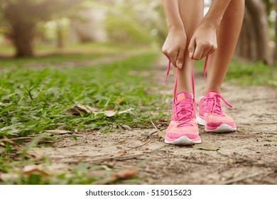 Caucasian Athletic Woman Tying Laces On Her Pink Running Shoes Before Jogging Standing On Footpath In Forest. Female Runner Lacing Her Sneakers While Doing Workout In Rural Area. Film Effect