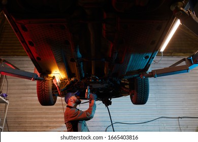 Caucasian Auto Mechanic Standing Under Car Fixing Its Parts, Horizontal Low Angle Shot, Copy Space