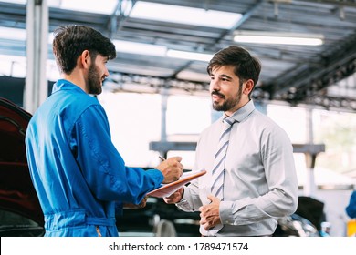 Caucasian Automotive Maintenance Mechanic Young Man Explain Car Condition To Male Customer In Garage At Auto Repair Shop, Technician Writing Document On Vehicle Checklist, After Service Concept