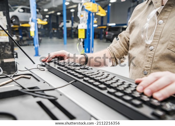 Caucasian Automotive Technician Checking Vehicle\
Database Documentation. Hands on Computer Keyboard Inside Auto\
Service Station.