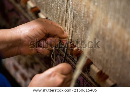 Caucasian Azerbaijani woman weaving a colorful traditional  carpet with traditional techniques on a loom by hands, an oriental ornament, closeup side view