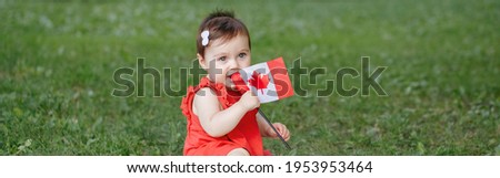 Caucasian baby toddler girl in red dress waving Canadian flag in park outdoors. Kid child citizen sitting on ground in park and celebrating Canada Day on 1st of July. Web banner header.