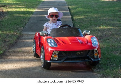 Caucasian baby in white hat riding in an electric convertible red sport car. child driving car on a summer day