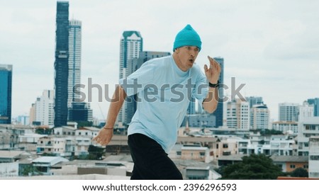 Caucasian B-boy dancer practicing street dancing at rooftop with city or urban. Motion shot of young man performing street dance by doing freeze pose. Break dance. Outdoor sport 2024. Endeavor.