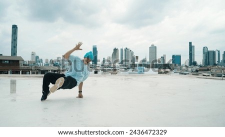 Caucasian B-boy dancer practicing street dancing at rooftop with city or urban. Motion shot of young man performing street dance by doing freeze pose or doing hand stand. Outdoor sport 2024. Endeavor.