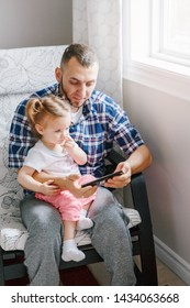 Caucasian bearded father dad sitting with daughter girl child watching cartoons on smartphone digital tablet together. Candid lifestyle family life. Single parent babysitting kid at home.