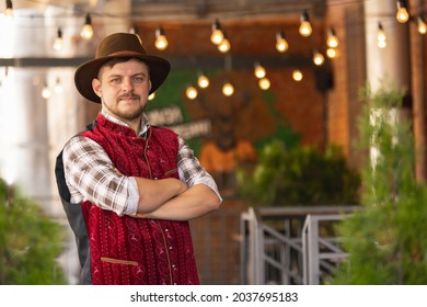 Caucasian Bearded Man, Owner Of Restaurant In Traditional Bavarian Festive Costume Greeting Customers, Visitors At Bar, Cafe, Pub. Oktoberfest, Fest, Joy, Fan, Ad Concept. Cozy Place, Outdoors