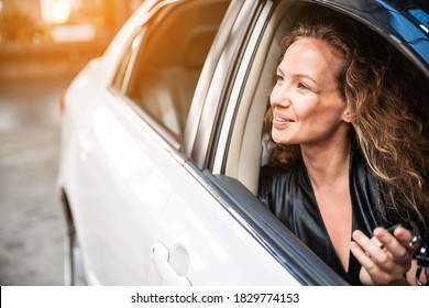 Caucasian beautiful female with a little smile sitting inside the car and looking outside the car window. Automobile rental and leasing business. Optimistic friendly woman. Focus on her eye.