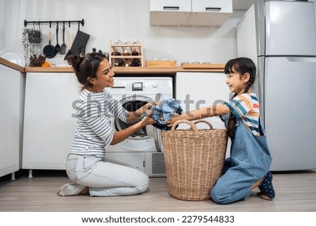 Caucasian beautiful mother teaching young daughter wash dirty clothes. Adorable little cute girl child help and learn from parent mom to put laundry in washer appliance at home. Domestic-Housekeeping.