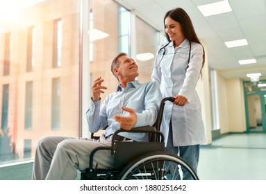 Caucasian beautiful  nurse taking care of a mature male patient sitting in a wheelchair at the hospital.  The woman smiles at the elderly man.