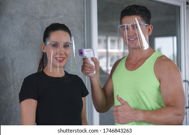 A Caucasian beautiful woman member wear face shield was checked with a temperature measuring device from a staff member before using the gym workout to prevent the outbreak of the virus - Powered by Shutterstock