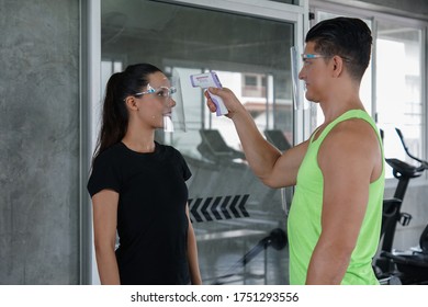 A Caucasian beautiful woman member wear face shield was checked with a temperature measuring device from a staff man before using the gym workout to prevent the outbreak of the virus - Powered by Shutterstock