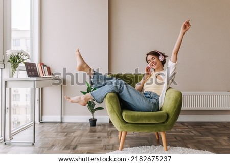 Caucasian beautiful woman smiling at home in headphones . Short brunette hair young girl wearing blue jeans listen music at home. Use technology, lifestyle concept  Stock foto © 