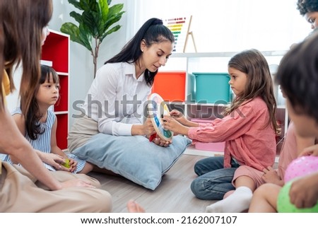 Caucasian beautiful young woman teacher teaching art to kids at school. Attractive Instructor master female explain and educate drawing and painting with student kindergarten pre school in classroom.