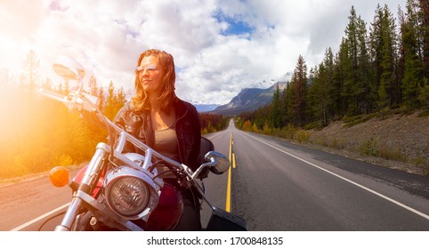 Caucasian Biker Woman On A Motorcycle On A Scenic Road In The Canadian Rockies. Image Composite. Background From Banff, Alberta, Canada.