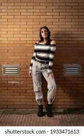 Caucasian black haired young woman wearing black and white striped t-shirt posing in front of a brown brick wall smiling