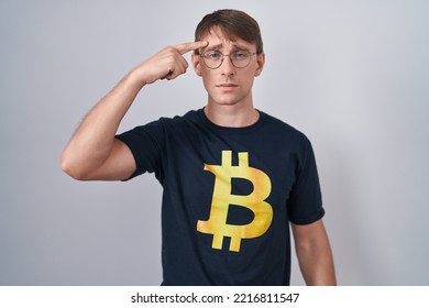 Caucasian Blond Man Wearing Bitcoin T Shirt Pointing Unhappy To Pimple On Forehead, Ugly Infection Of Blackhead. Acne And Skin Problem 