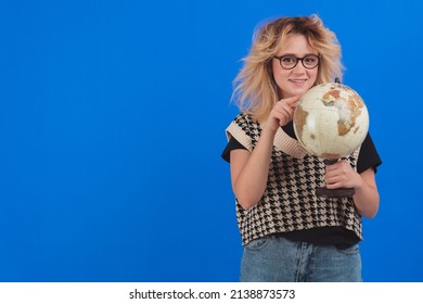 Caucasian Blonde Girl With A Globe. Copy Space. Isolated Studio Shot. Blue Background. High Quality Photo