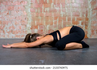 Caucasian blonde yoga woman in black clothes practicing sport pose extended puppy indoor