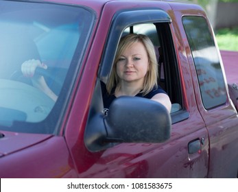 Caucasian Blonde Young Woman Driving In The Cab Of A Red Pickup Truck
