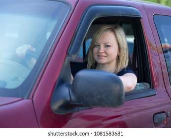 Caucasian Blonde Young Woman Driving In The Cab Of A Red Pickup Truck
