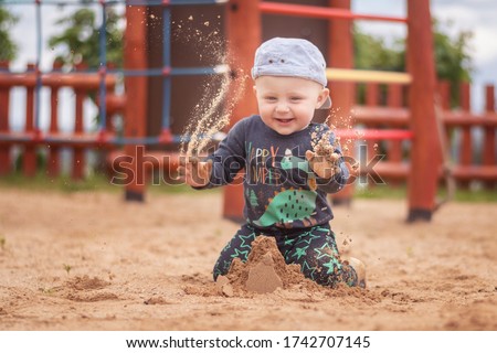 Caucasian boy in baseball cap playing on sand at playground. An 11 month old boy throws sand in the air.