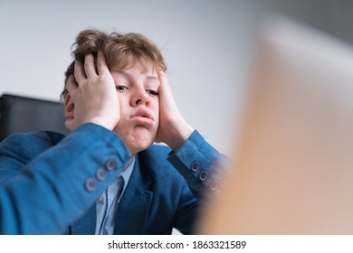 Caucasian Boy In Blue School Uniform Is Sick And Tired Of His Online Classes. He Is Almost Looking To The Screen Without Any Interest, He's Pouting His Lips And Holding His Head.