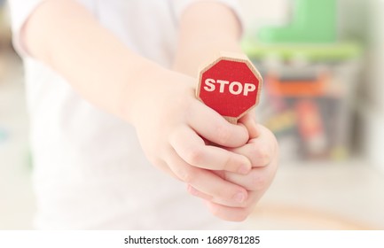 Caucasian Boy Is Clutching In His Palms And Holding A Close-up Wooden Road Stop Sign From The Children's Kit In A Bright Children's Room. Teaching Children The Rules Of The Road, Child Safety Concept