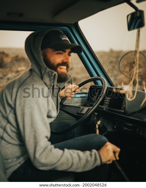 Caucasian boy driving a vintage van\
around Lanzarote island in February with volcanic landscape and\
dream catcher as decoration while the sun hides on the\
horizon