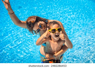 Caucasian boy expressing that he is having fun with his mother in the swimming pool raising thumbs up - Powered by Shutterstock