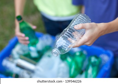 Caucasian boy and girl putting clear and green bottles and metal cans in recycling blue bin outside in yard - Powered by Shutterstock