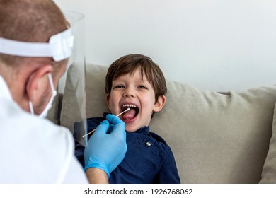 Caucasian Boy Having PCR Test During Coronavirus Pandemic. Doctor Takes A Cotton Swab Test From Child Mouth To Analyse For Covid-19. Pediatrician Using A Swab To Take A Sample From A Patient's Throat.