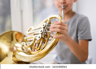 Caucasian Boy Learns To Play The Horns, A Child Plays A Wind Musical Instrument. Light Window, Real Interior.