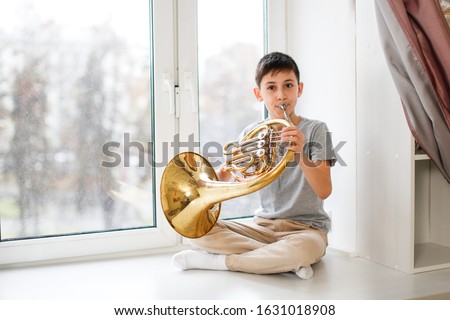 Caucasian boy learns to play the horns, a child plays a wind musical instrument. Light window, real interior.