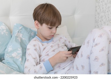 Caucasian boy lies in bed and plays phone, boy in pajamas morning and afternoon. Free time for games - Powered by Shutterstock
