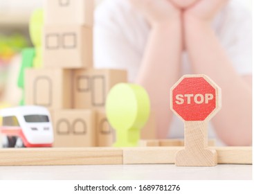 Caucasian Boy Is Playing Stop Road Sign On The Background Of The Children's Kit Of A Wooden Toy City. Railway In The Children's Room. Teaching Children The Rules Of The Road, Child Safety Concept