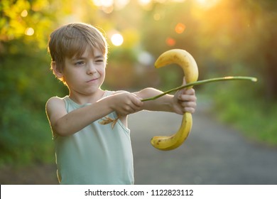 Caucasian boy plays  on the street in the summer day on sunset and represents archery. Bananas instead of bow for shooting. Horizontal shot. - Powered by Shutterstock