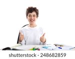 Caucasian boy is smiling and holding thumbs up while sitting at desk with books school supplies
