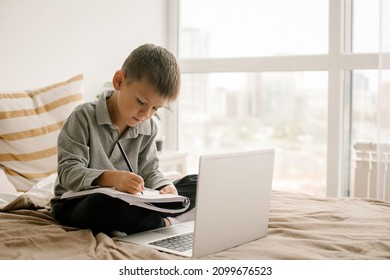 Caucasian Boy Student Studing From Home Virtual Classroom Using Laptop For Distance Study. Cute Boy 7 Years Old Writing In A Workbook