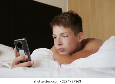 Caucasian boy teenager lying on pillow and enjoying using smartp