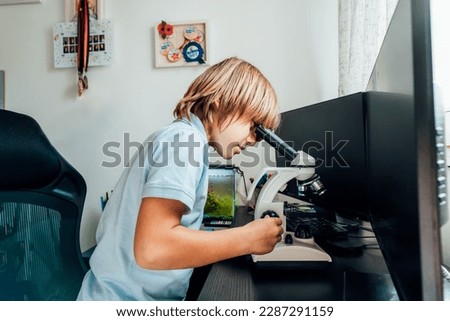 Caucasian boy using a microscope at home at his study place. Child curiosity, thirst for knowledge, home learning experience, home remote education concepts. Selective focus.