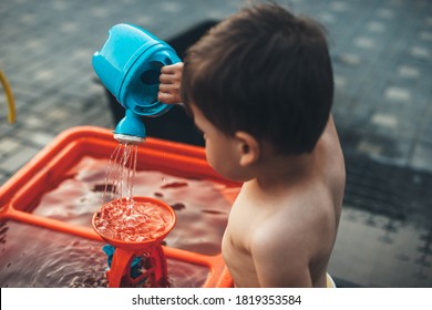 Caucasian Boy Watering A Toy While Playing Outside Undressed In A Summer Day