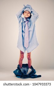 Caucasian Boy Wearing His Dad's Shirt, Jeans And Tie On Light Background. He Is Wearing Big Adult Size Clothes Which Are Too Big For Him.