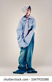 Caucasian Boy Wearing His Dad's Shirt, Jeans And Tie On Light Background. He Is Wearing Big Adult Size Clothes Which Are Too Big For Him.