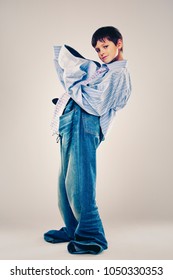 Caucasian Boy Wearing His Dad's Shirt, Jeans And Tie On Light Background. He Is Wearing Big Adult Size Clothes Which Are Too Big For Him.